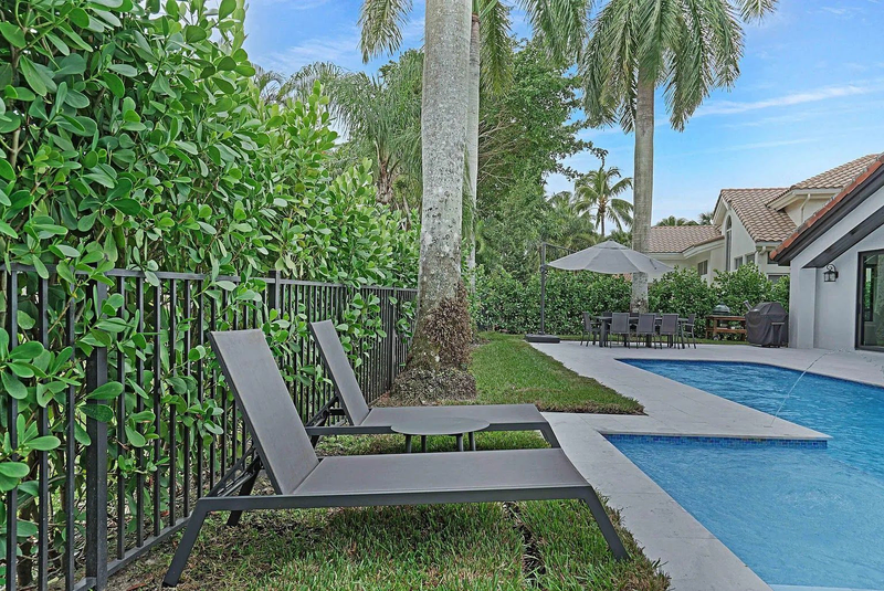 Poolside lounge chairs beside tropical backyard pool