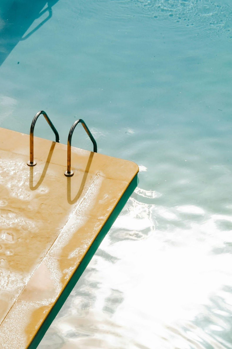 Pool ladder on sunlit deck beside turquoise water