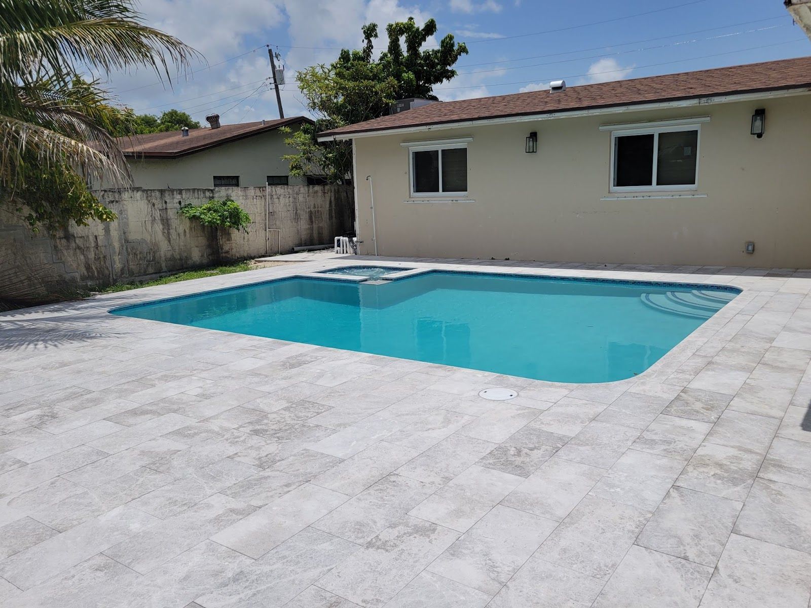 Backyard pool with spa, tiled deck and beige house exterior
