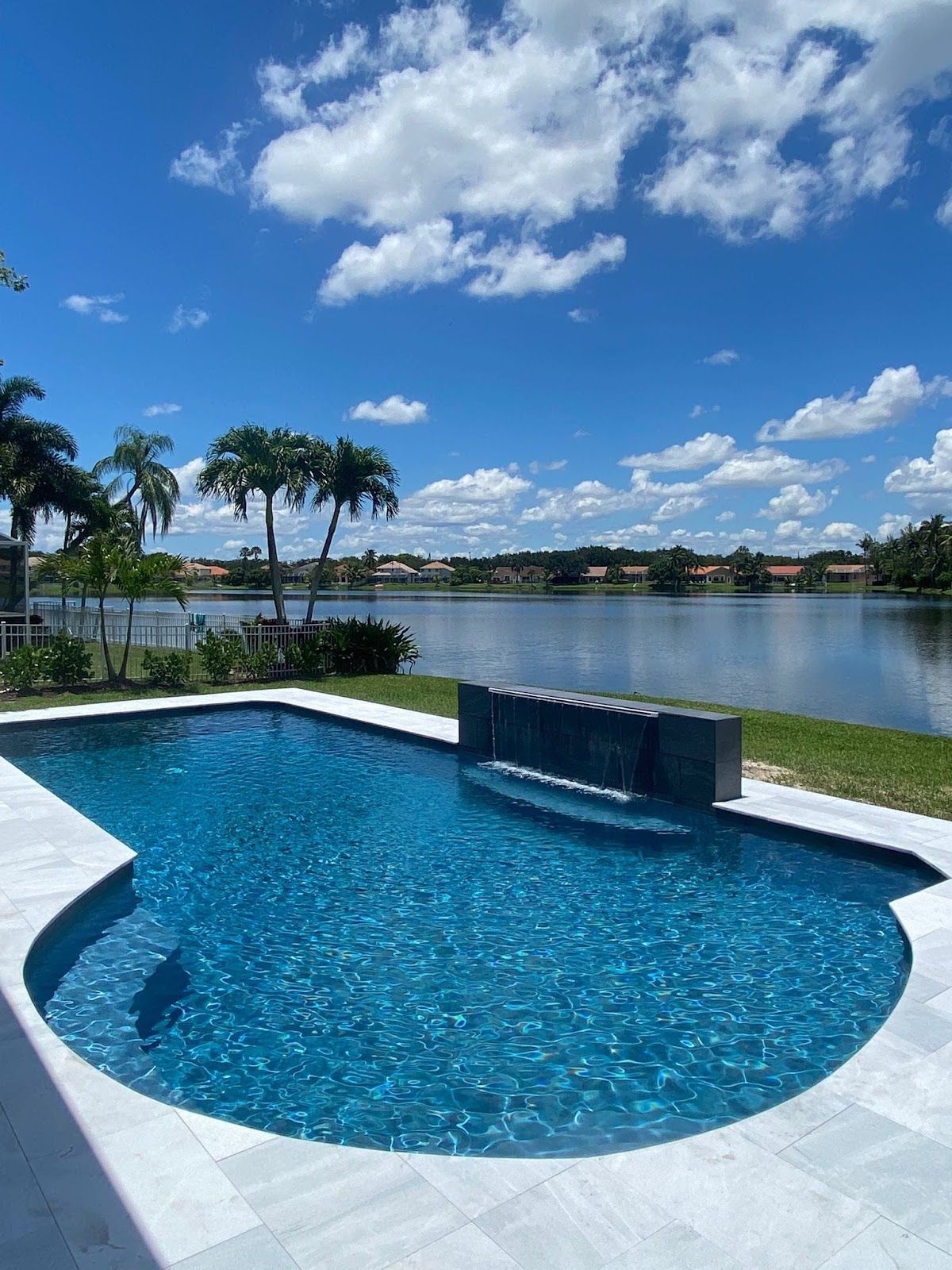Modern backyard pool overlooking lake with palm trees view.