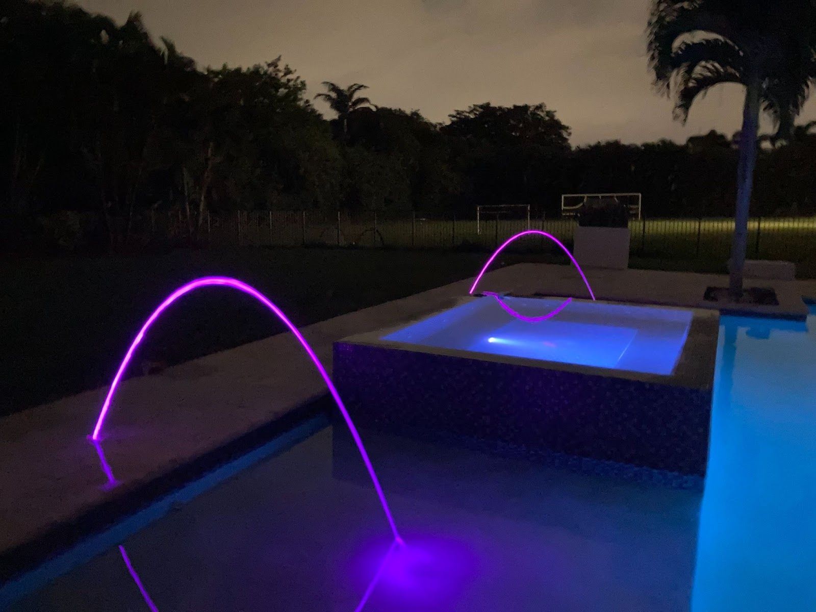 Night pool with purple LED water features and glowing spa jets