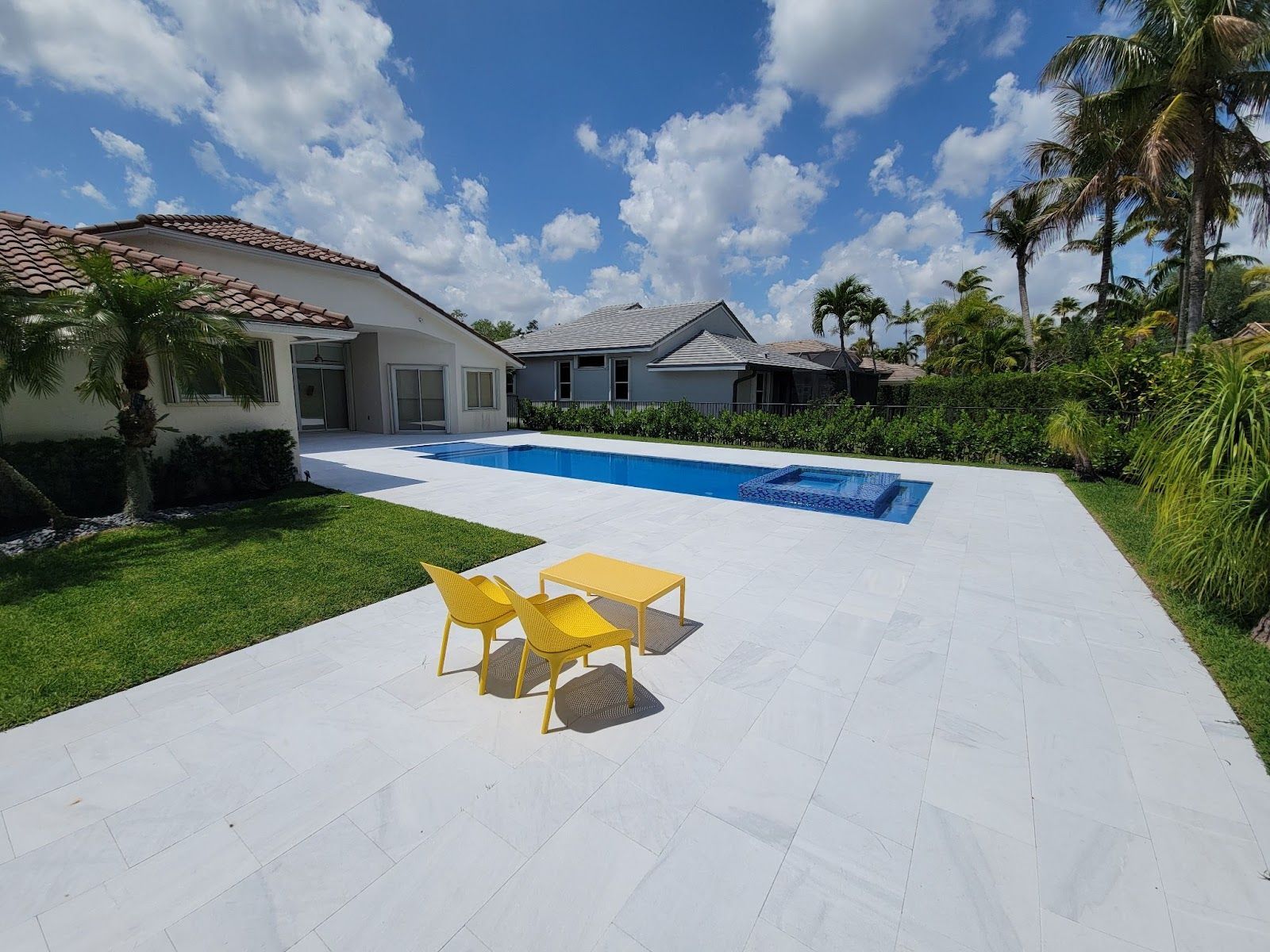 Modern backyard pool with spa, tiled patio and yellow chairs