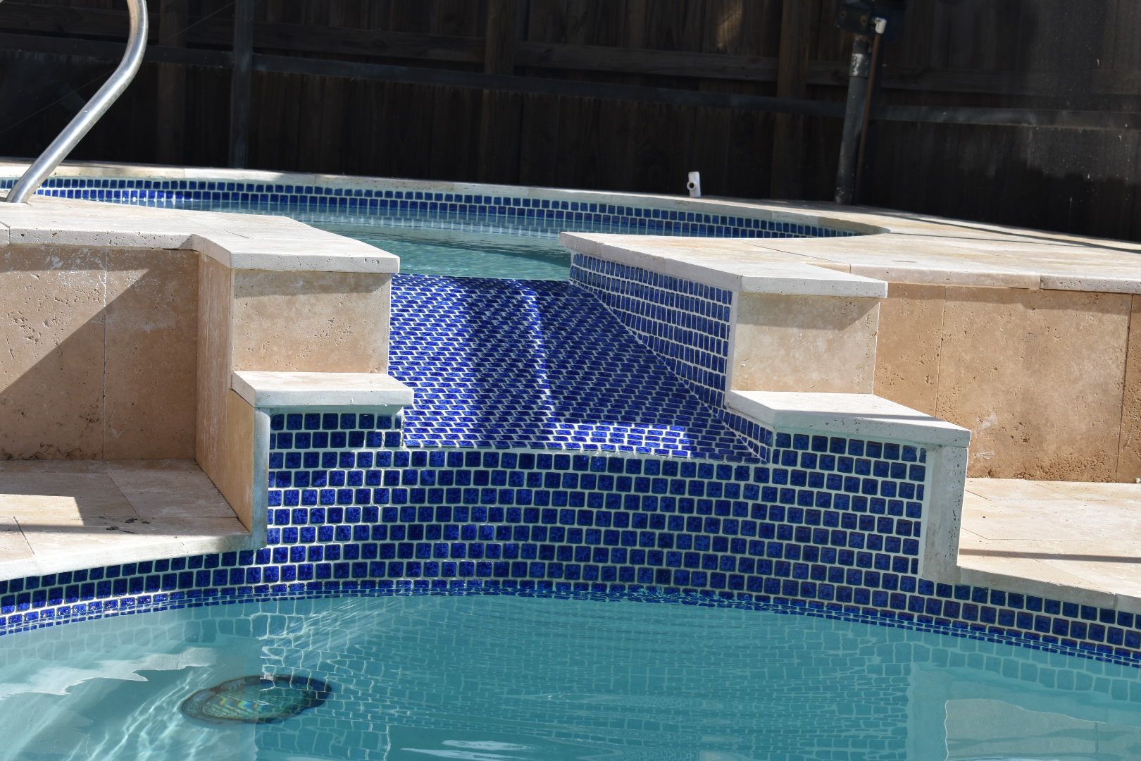 Swimming pool spa with blue tile spillway and stone coping